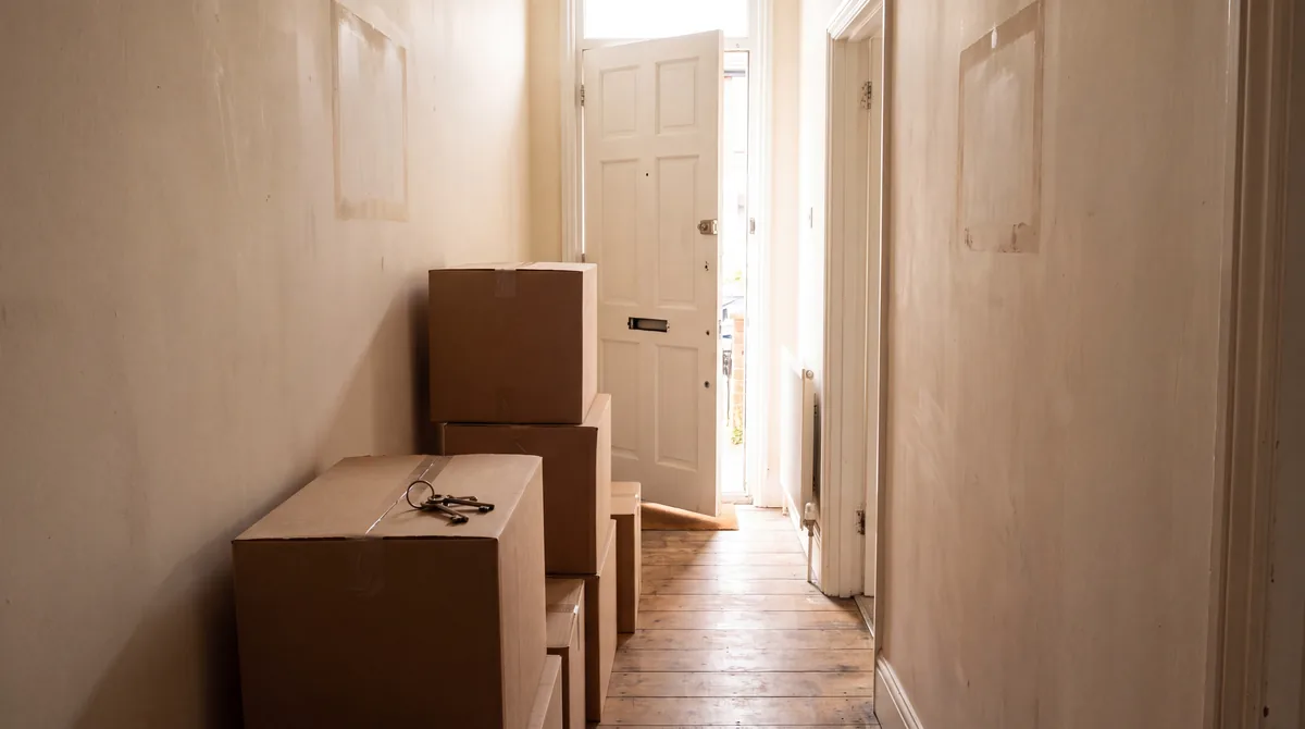 Cardboard moving boxes stacked in the hallway of an empty British home with morning light through the front door